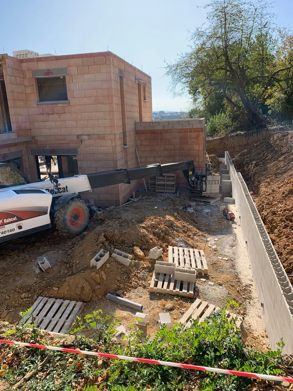 Terrassement et fondations le long d’une maison en brique en construction
