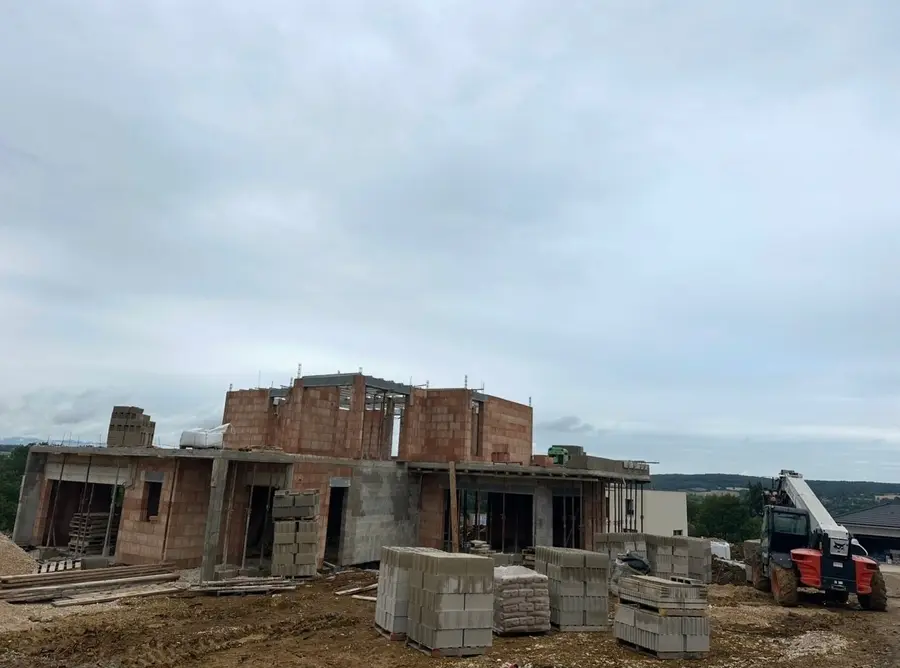 Maison en brique en construction avec palettes de blocs et chariot télescopique