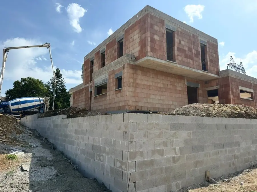 Maison cubique en brique sur soubassement en blocs béton, pompe à béton en arrière-plan